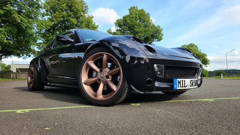 Schwarzer Smart Roadster 452 mit roségoldenen Felgen auf einer Landstraße